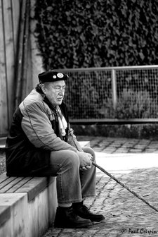 Old Man Sitting on a Wall with a stick